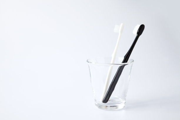 白色的黑色牙刷放在玻璃化妆品里，孤立在白色的背景上图片下载