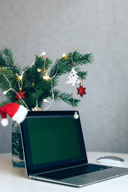 桌上放着一台打开的笔记本电脑，旁边是一棵装饰着球和花环的圣诞树。工作场所的新年和圣诞气氛图片下载