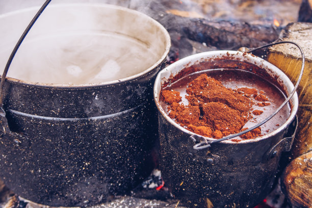 用野营用的壶烧着咖啡和热水沏茶或炖菜。户外热气腾腾的食物。野生动物生活方式烹饪美食，Copyspace库存照片图片下载