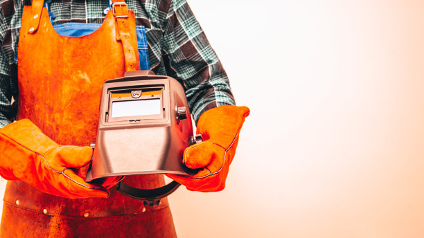 一个焊工穿着防护服，戴着手套，胳膊下夹着一个焊接面罩。特写，笔记空间，炽热的色彩图片下载