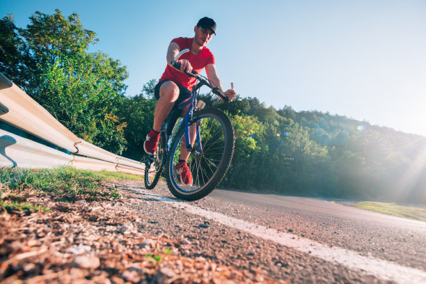身材健美的男自行车手骑自行车自行车在沥青路上在日落时，太阳通过他的车轮。图片下载