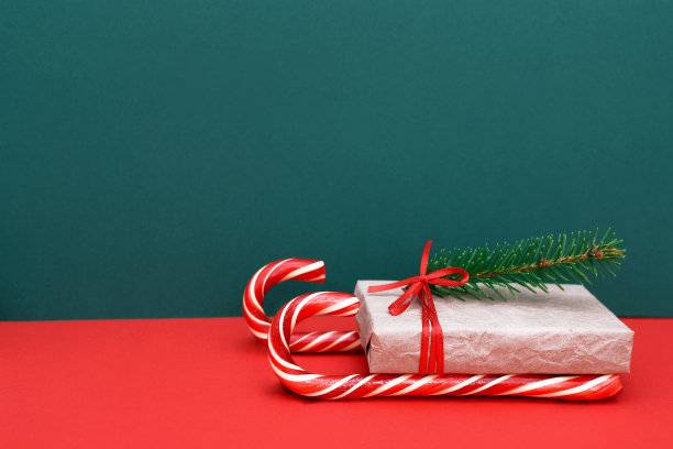 圣诞老人的自制雪橇，由红色和白色条纹糖果在一根手杖的形式和一个礼品盒与一个红色丝带蝴蝶结和一个云杉树枝，传递祝贺和礼物给家人和朋友，复制空间。图片下载