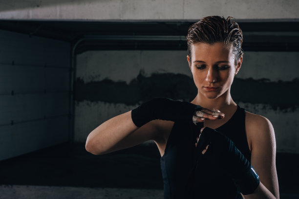 这张照片是一名专注的年轻女子在一间车库里准备她的黑色拳击绷带。图片下载