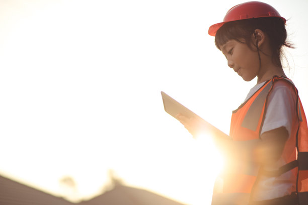 亚洲小女孩头上戴着安全帽，手里拿着平板电脑在建筑工地上图片下载