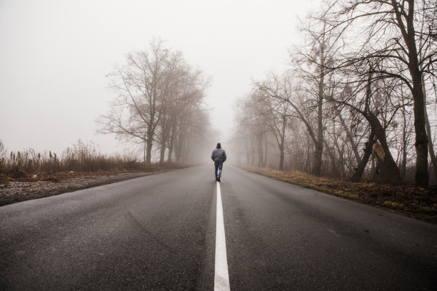 一个人走在雾蒙蒙的秋天风景中。孤独的人在雾中行走。乡村景观与道路在晨雾。温暖的秋天的颜色。黑暗神秘的背景图片下载