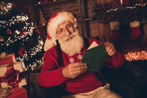 可爱的圣诞老人的照片穿着红色的服装微笑着读信在屋内的房间图片下载