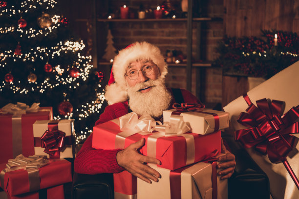 照片正面圣诞老人抱大堆礼物盒戴眼镜帽子套衫在北极办公室室内图片下载