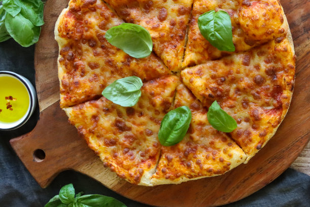 整幅图片:切好的玛格丽塔披萨放在圆形木砧板上，融化的金色水牛马苏里拉奶酪，浓郁的番茄marinara酱和新鲜的罗勒叶，蓝色茶巾，橄榄油，木纹背景图片下载