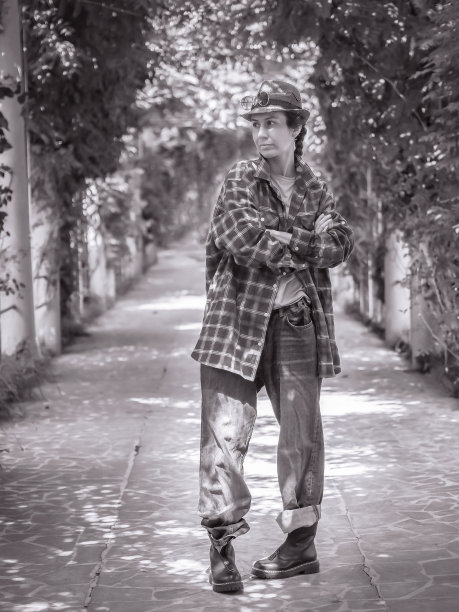 一个女孩戴着帽子，穿着宽松的服装，双腿弯曲，双臂交叉站在公园的一条小巷里。黑白照片图片下载