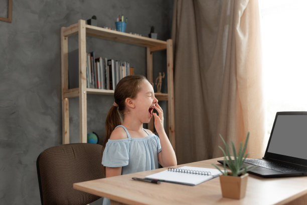 一个女学生坐在桌旁做家庭作业时打哈欠。一名疲惫的女学生远程在线学习，然后睡着了。小学的学生。乏力图片下载