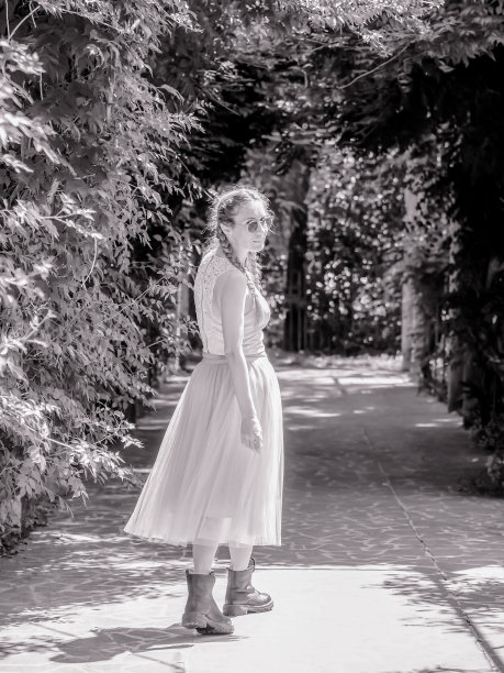 一个穿着薄纱裙子和粗糙靴子的女士走在公园的小巷里回头看。黑白照片图片下载