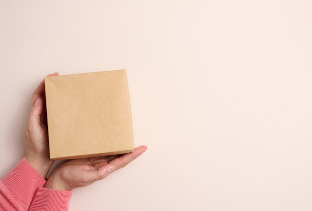 女性手握方形纸板箱在米色背景上，俯视图图片下载