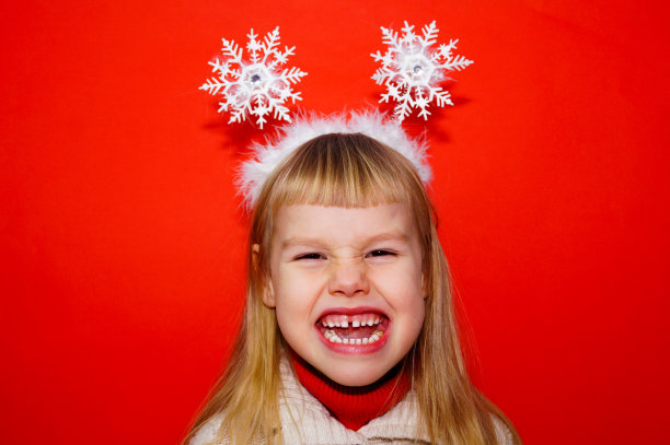 这个小女孩在感情上很生气，表达了不满。红色的背景。肖像。女孩头上的圣诞装饰。图片下载