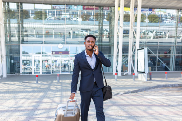 非裔美国旅游商人以行李为背景走公共交通大楼，后视镜西装革履的男子旅行城市。在机场候机楼提手提箱的商务旅客图片下载