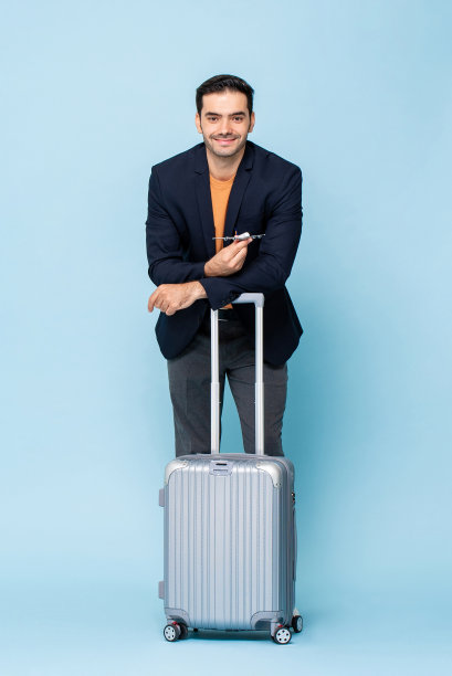 年轻的微笑英俊的男子站与一个手提箱和持有飞机模型在孤立的浅蓝色工作室背景图片下载