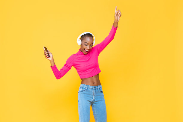 快乐的非裔美国妇女的肖像戴着耳机听音乐和跳舞在彩色的黄色孤立的背景图片下载