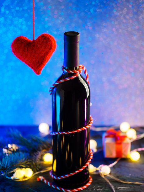 情人节快乐概念。一瓶红酒，一颗红色编织的心，一个礼品盒和一个带有复制空间的霓虹背景图片下载