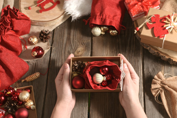 女人的手拿着圣诞礼物放在木桌上，旁边是其他玩具和礼物。真实的圣诞特写照片。为假期做准备。工艺礼品。DIY。出现。舒适的在家度假图片下载