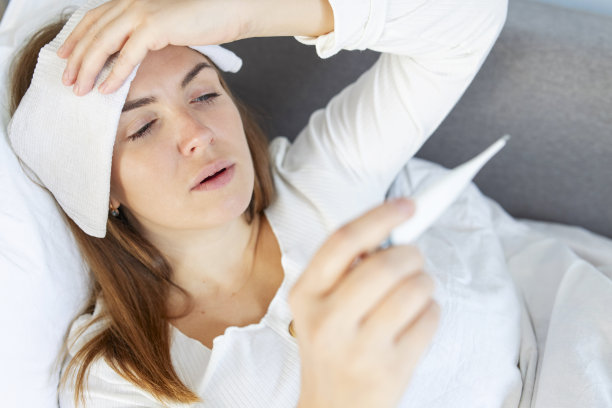 患有流感或covid-19的妇女躺在床上，她正在用温度计测量自己的体温，并触摸自己的额头。生病的女人图片下载