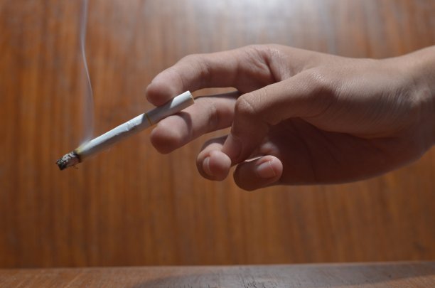 在木制背景下，男性手握香烟的姿势图片下载