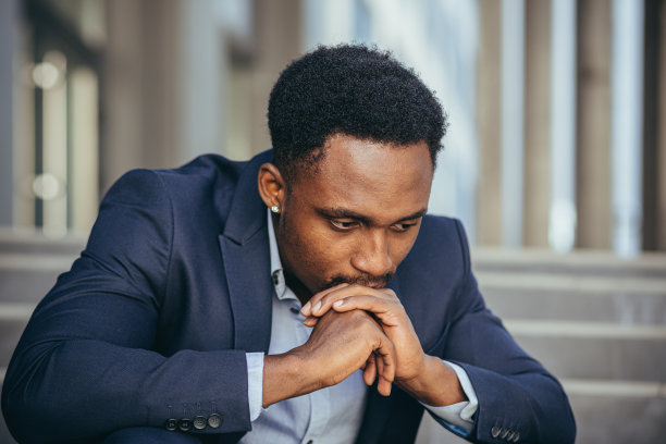 西装革面的非洲裔美国商人沮丧地从工作中得到坏消息，沮丧地坐在楼梯上，特写肖像照片图片下载
