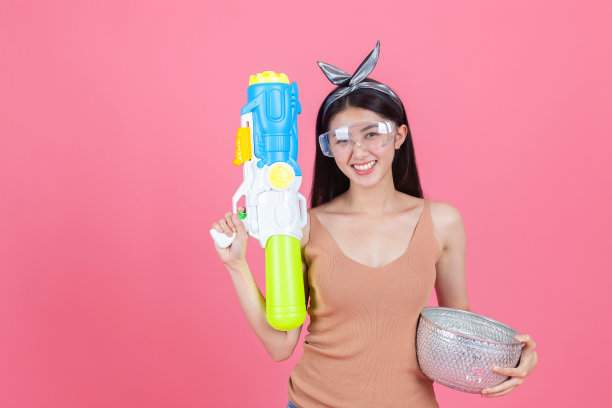 亚洲滑稽女孩拿着水枪在粉红色的背景。在夏天玩水。图片下载