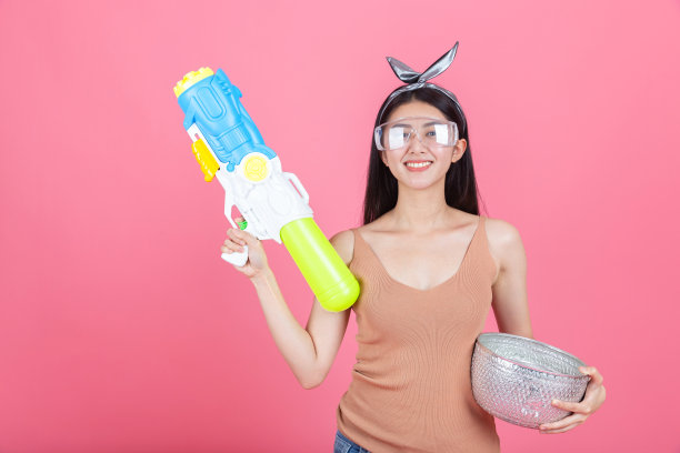 亚洲滑稽女孩拿着水枪在粉红色的背景。在夏天玩水。图片下载