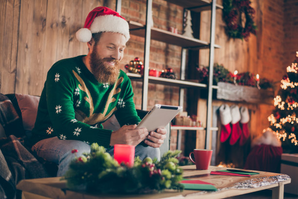 照片的自由职业者姜家伙坐在舒适的椅子浏览平板电脑穿圣诞帽毛衣装饰的家在室内图片下载