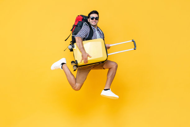 年轻兴奋的白人男性游客的肖像，行李在半空中跳跃，孤立在彩色工作室的黄色背景图片下载