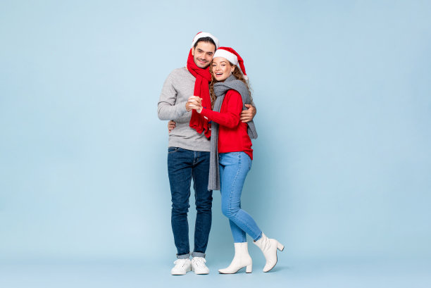 完整的肖像快乐的白人夫妇在圣诞节服装抱着彼此在浅蓝色独立的工作室背景图片下载