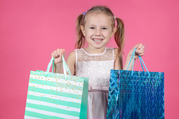 有趣的女孩穿着派对礼服和购物袋孤立在粉红色的背景图片下载