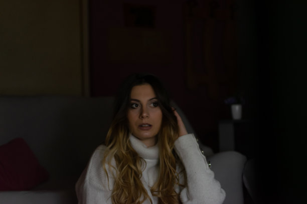 一个漂亮的年轻女人坐在家里的地板和沙发上，在黑暗中看电影，吃爆米花，微笑，享受她的空闲时间和周末活动的高清照片。图片下载