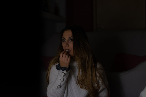 一个漂亮的年轻女人坐在家里的地板和沙发上，在黑暗中看电影，吃爆米花，微笑，享受她的空闲时间和周末活动的高清照片。图片下载