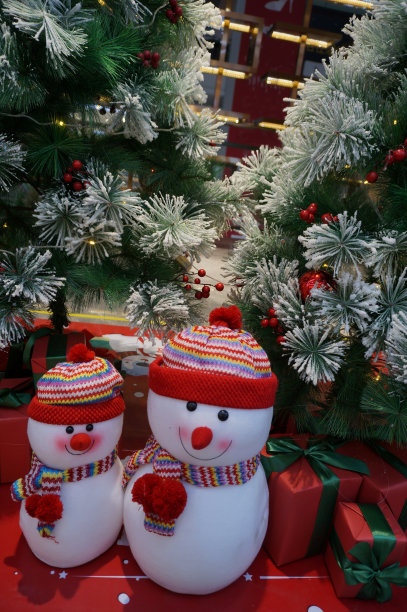 圣诞节装饰有两个雪人，穿着红色的羊毛外套，戴着红色的围巾和红色的圣诞帽。在一棵绿色的圣诞树上。图片下载