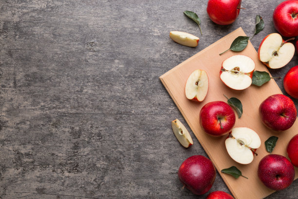 桌上放着新鲜的红苹果和绿叶。用刀切砧板。俯视图图片下载