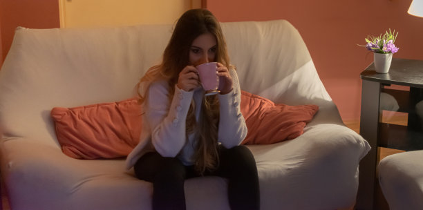 一个漂亮的年轻女人坐在家里的地板和沙发上，在黑暗中看电影，吃爆米花，微笑，享受她的空闲时间和周末活动的高清照片。图片下载