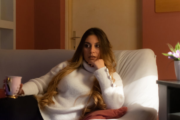 一个漂亮的年轻女人坐在家里的地板和沙发上，在黑暗中看电影，吃爆米花，微笑，享受她的空闲时间和周末活动的高清照片。图片下载