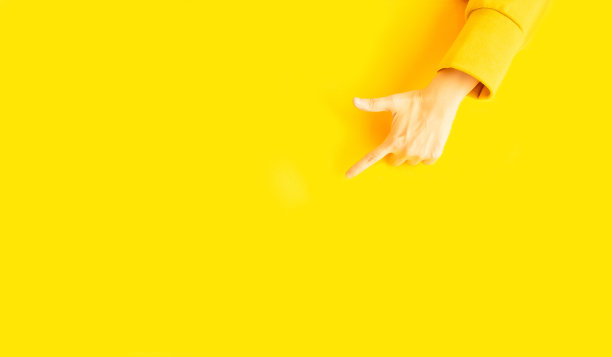 女人的手用黄色的长袖毛衣用食指指向复制空间，用于广告宣传或黄色背景上的文字图片下载