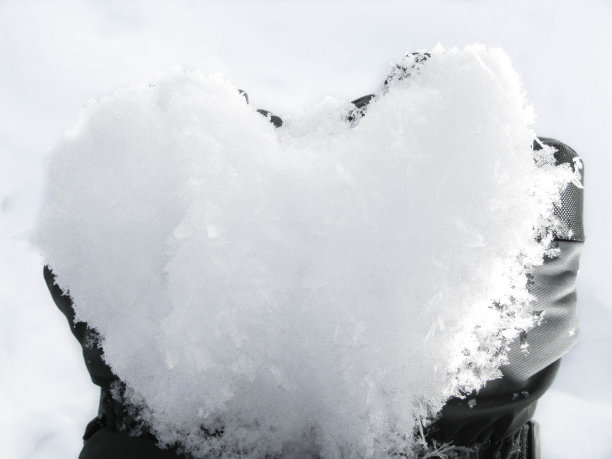 在白雪的背景下，手拿着一个心形的雪球。浪漫的姿态和象征图片下载