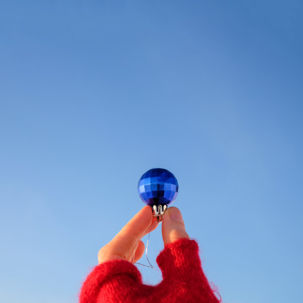 手握红色手套的圣诞球在蓝天背景，正方形照片与复制空间图片下载