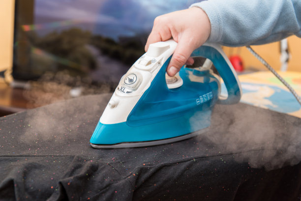 一个妇女的手在她的家里熨一件黑色的t恤。图片下载