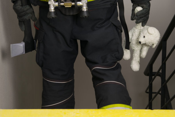 一名消防队员走下楼梯，手里拿着一个泰迪熊玩具和一把用来开门的斧头图片下载