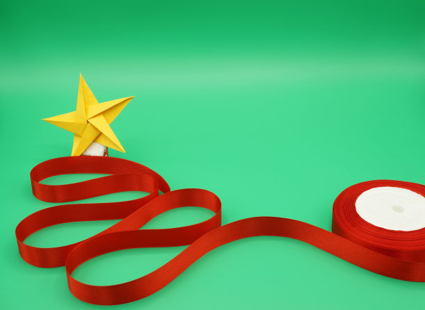 圣诞节庆祝活动的主题。绿色背景，概念形状的圣诞树被红色丝带和圣诞星星折叠在金色的纸。手工制作的孩子气的背景。图片下载