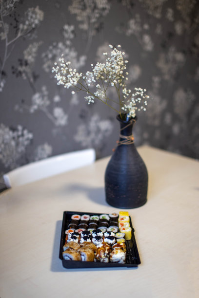 一套寿司，卷在桌上。寿司送回家，花瓶里装着白花干花。寿司配米饭和紫菜。日本食品卷的特写镜头。图片下载