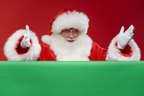 一个惊讶的圣诞老人俯视着他面前的一个色度键，他站在一个红色背景的工作室里图片下载