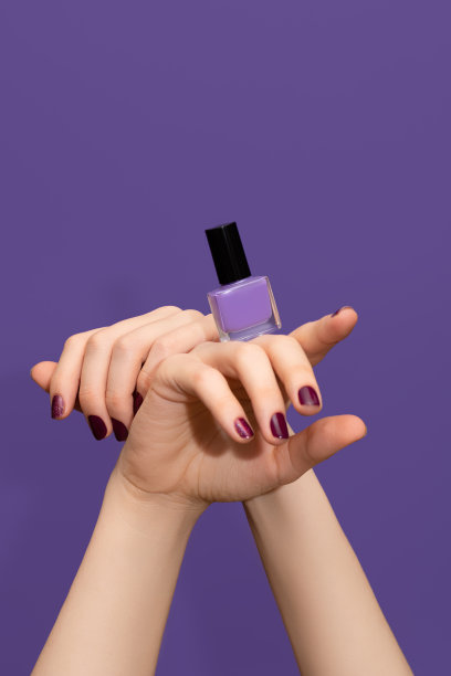 女性双手红色指甲设计。亮红色指甲油修指甲。女性的手在紫色的背景上涂着紫色的指甲油。图片下载