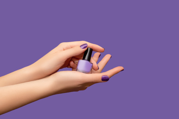 女性的手有紫色的指甲设计。亮紫色指甲油修指甲。女性的手在紫色的背景上涂着紫色的指甲油。图片下载