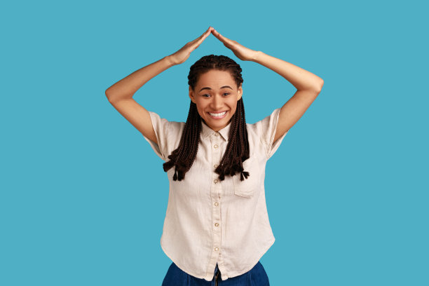 站着的女人举起双手，露出屋顶的姿态，满意地微笑着，梦想着房子。图片下载