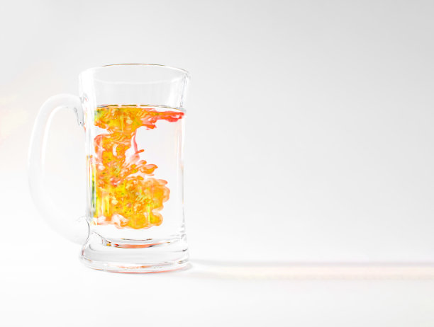 一杯水与黄色墨水滴入，旋转和扭曲，在玻璃杯中隔离的白色，工作室照片拍摄，化学或科学实验的概念图片下载