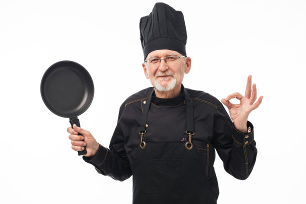 灰色胡子的老头穿着黑色围裙，戴着帽子，手里拿着平底锅，在白色背景下愉快地看着镜头图片下载